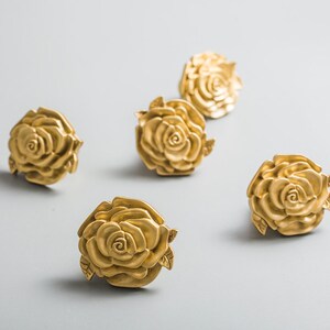 May include: Five gold-toned rose-shaped drawer pulls. Each pull features a detailed rose design with leaves.