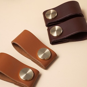 Op de afbeelding: Vier lederen ladegrepen met messingknoppen. Twee zijn van bruin leer en twee zijn van bruin leer.