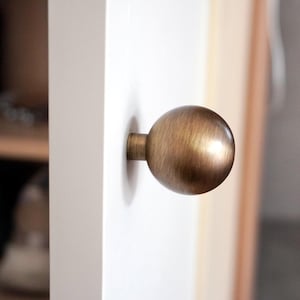 May include: A round, brushed brass cabinet knob with a slightly oval shape.