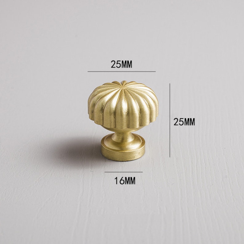 May include: A gold-coloured cabinet knob with a ribbed, rounded top and a pedestal base. The knob measures 2.5cm in height and width, and 1.6cm in diameter at the base. The hardware is designed for furniture and home decor.