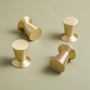 May include: Four gold-toned cabinet knobs with a cone shape. The knobs have a smooth, polished finish.