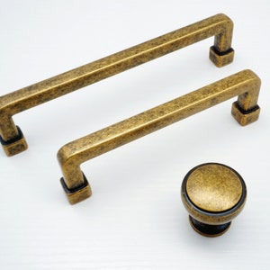 Puede incluir: Dos tiradores de armario de oro antiguo con extremos cuadrados y un pomo redondo con un acabado similar.