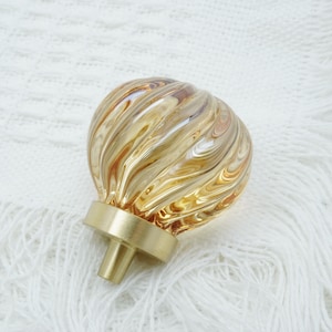 May include: A gold and amber glass cabinet knob with a swirl pattern. The knob has a brass base.