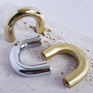 May include: Three U-shaped cabinet pulls in different finishes: polished brass, brushed nickel and satin brass.