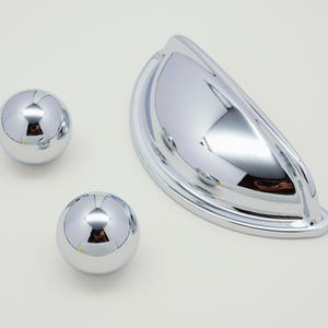 Könnte beinhalten: Drei verchromte Schrankknöpfe, zwei runde und ein halbrunder.