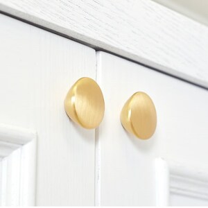 Op de afbeelding: Twee ronde kastknoppen in een geborstelde gouden afwerking.