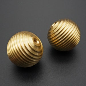 Puede incluir: Dos pomos decorativos redondos de color dorado con una superficie texturizada y estriada.