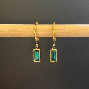 May include: Gold hoop earrings with a dangling rectangular blue gemstone.