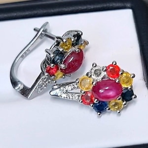 Può includere: Un paio di orecchini d'argento con un gruppo di pietre preziose colorate, tra cui rosso, giallo, blu e bianco. Gli orecchini hanno una chiusura a leva.