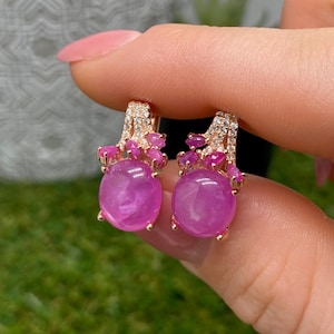 Op de afbeelding: Een paar oorbellen van roségoud met grote, ronde, roze cabochon-geslepen stenen aan de basis. Elke oorbel is versierd met kleinere, marquise-geslepen roze stenen en kleine, heldere, fonkelende pavé-gezette kristallen op de metalen structuur.