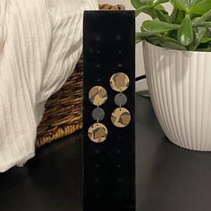 Puede incluir: Un par de pendientes colgantes con dos discos redondos de arcilla con estampado marrón y negro en cada pendiente.