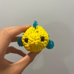 May include: A yellow rubber band fish with blue fins and black eyes. The fish is made with a loom.