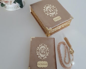 May include: A gold velvet box with an intricate design and the words "Eid Mubarak" on the front. The box is open and contains a smaller gold velvet book with the same design and text. A gold prayer bead necklace with a tassel is also included.