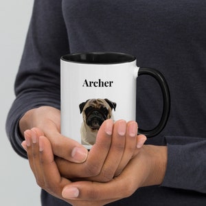 May include: White ceramic mug with a black rim and handle. The mug has a black and white illustration of a pug dog and the name "Archer" printed on the front.