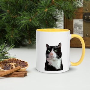 May include: A white ceramic mug with a yellow rim and handle. The mug features a black and white cat with green eyes.