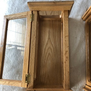 K&ouml;nnte beinhalten: Ein Holzausstellungsvitrine mit einer Glast&uuml;r und Messing Scharnieren. Die Vitrine ist offen und leer.