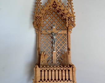 May include: A wooden wall-mounted crucifix with a detailed gothic design. The crucifix features a silver-toned Jesus figure and a decorative shelf below.