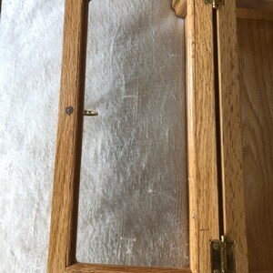 K&ouml;nnte beinhalten: Ein Holzausstellungsvitrine mit einer Glasfront und Messing Scharnieren. Die Vitrine ist offen und das Glas ist sichtbar.