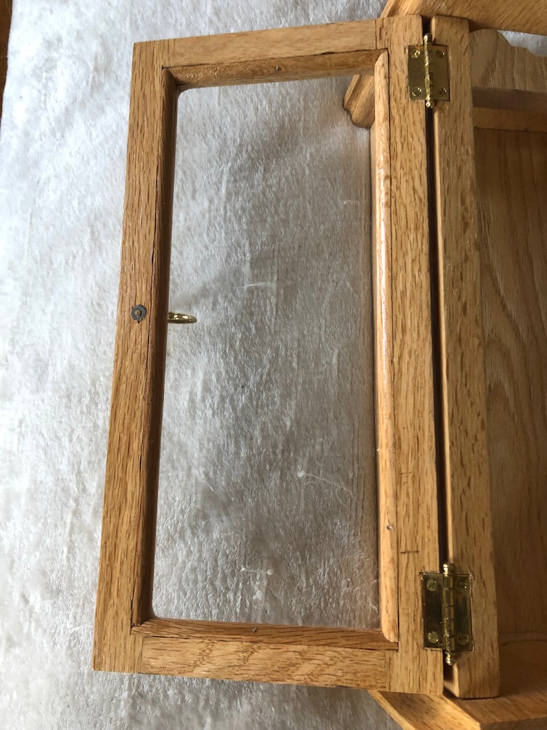 K&ouml;nnte beinhalten: Ein Holzausstellungsvitrine mit einer Glasfront und Messing Scharnieren. Die Vitrine ist offen und das Glas ist sichtbar.