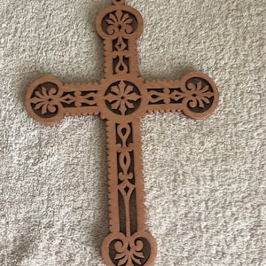 May include: A wooden cross with intricate cut-out designs. The cross is made of light brown wood and has a heart-shaped bottom.