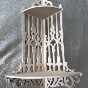 Op de afbeelding: Een houten hoekplank met ingewikkelde uitsnijdingen en een decoratief ontwerp. De plank heeft twee niveaus en is gemaakt van licht hout.