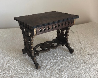 May include: A small, intricately carved wooden table with a dark brown finish. The table has a rectangular top and decorative legs.