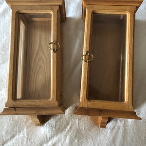 K&ouml;nnte beinhalten: Zwei Holzauslagen mit Glast&uuml;ren und Messinggriffen. Die Auslagen sind an der Wand montiert und haben ein dekoratives Design am Boden.