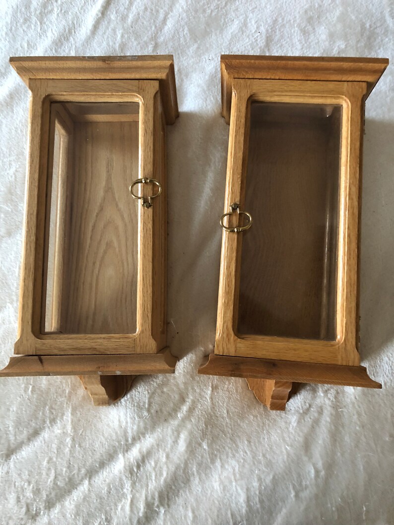 K&ouml;nnte beinhalten: Zwei Holzauslagen mit Glast&uuml;ren und Messinggriffen. Die Auslagen sind an der Wand montiert und haben ein dekoratives Design am Boden.