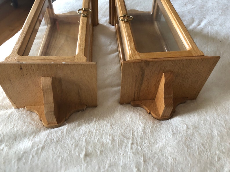K&ouml;nnte beinhalten: Zwei Holzauslagen mit Glasfronten und Messingbeschl&auml;gen. Die Auslagen haben eine helle Holzoptik und sind auf einer wei&szlig;en Oberfl&auml;che montiert.
