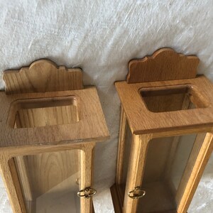 K&ouml;nnte beinhalten: Zwei Holzauslagen mit Glasfronten und verzierten Holzoberteilen. Die Auslagen sind aus hellbraunem Holz gefertigt und haben ein schlichtes Design.