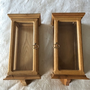 K&ouml;nnte beinhalten: Zwei Holzauslagen mit Glasfronten und Messinggriffen. Die Auslagen sind an einer Wand montiert und haben ein schlichtes, traditionelles Design.