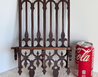 May include: A dark brown wooden wall shelf with a gothic design. The shelf has a small ledge and three decorative points at the bottom. The shelf is about 12 inches tall and 6 inches wide.