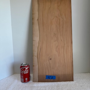 Op de afbeelding: Een rechthoekige lichtbruine houten plank met een natuurlijke boomkant aan de linkerkant. Een klein blauw stukje tape met de tekst 1/8" A is onderaan in het midden bevestigd. Een rood aluminium frisdrankblikje staat links van de houten plank.