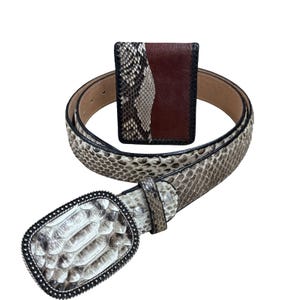 Könnte beinhalten: Ein Schlangenleder-Gürtel mit dekorativer Schnalle und eine passende Schlangenleder- und braune Leder-Geldbörse. Der Gürtel hat eine hellbraune Lederunterseite und eine silberfarbene Schnalle. Die Geldbörse hat eine Schlangenleder- und eine braune Lederplatte.