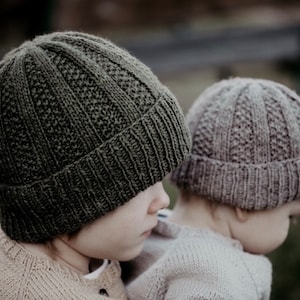 Könnte beinhalten: Zwei Kinder tragen Strickmützen. Die Mütze links ist dunkelgrün und die Mütze rechts ist hellbraun.