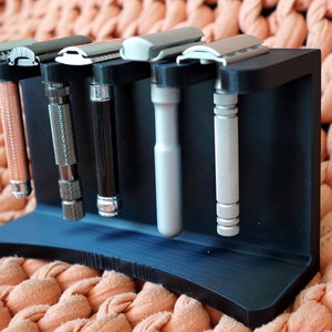 May include: A black plastic stand with five silver safety razors. The stand has a curved base and is designed to hold the razors upright.