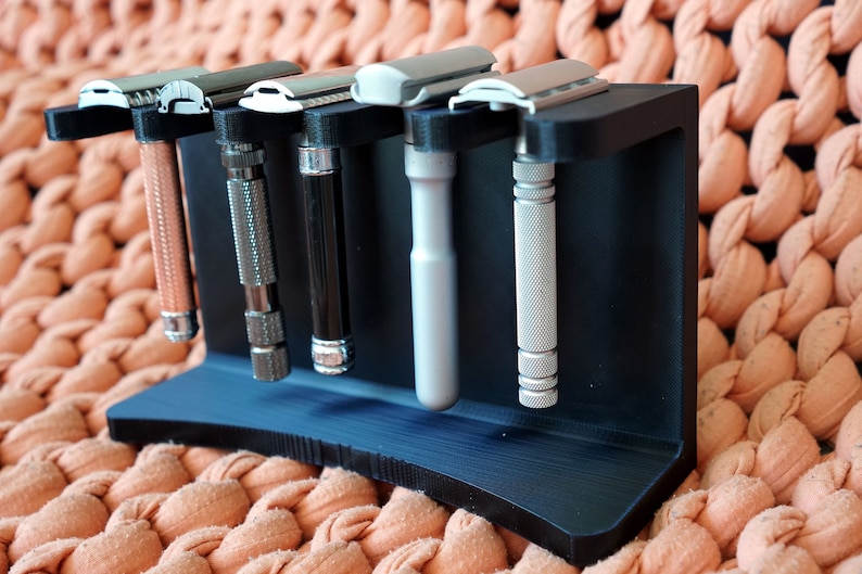 May include: A black plastic stand with five silver safety razors. The stand has a curved base and is designed to hold the razors upright.