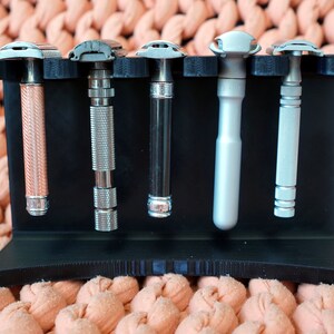 May include: A black plastic stand with five silver and rose gold safety razors. The stand has a textured surface and is designed to hold the razors upright.