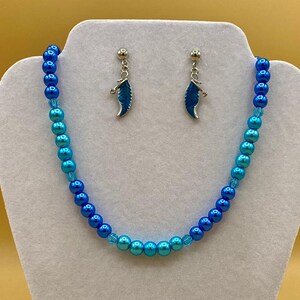 May include: A blue and turquoise ombre beaded necklace with silver feather earrings.