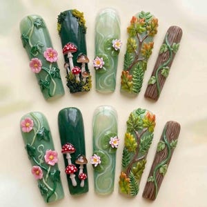 Könnte beinhalten: Zehn künstliche Fingernägel mit von der Natur inspirierten Designs. Die Nägel zeigen detaillierte Miniaturkunst, darunter rosa Blumen, Pilze, Seerosen und Äste. Die Farbpalette umfasst Grüntöne, Braun und Rosa.