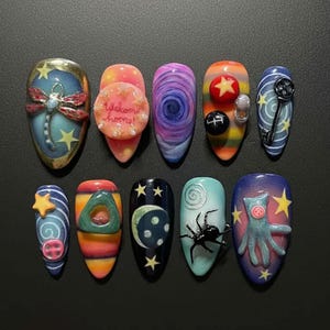 Könnte beinhalten: Ein Set von zehn künstlichen Nägeln in ovaler, langer Form, jeweils mit einzigartigem Design. Die Nagelkunst zeigt eine Libelle, einen Kuchen mit dem Text "welcome home!", eine wirbelnde Galaxie, Sterne, einen Schlüssel und eine Spinne.