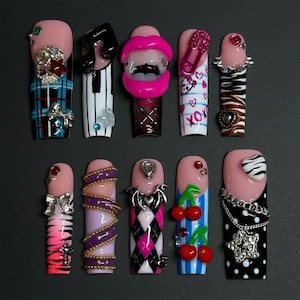 Könnte beinhalten: Eine Sammlung von zehn langen, verzierten Kunstnägeln. Designs umfassen einen Totenkopf, Noten, rosa Lippen, ein Hello Kitty-Thema, Zebrastreifen, Schleifen, Argyle, Kirschen und einen Stern. Jeder Nagel hat ein anderes Farbschema und Verzierungen.