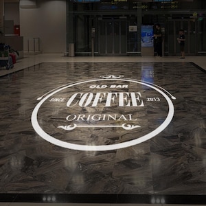 May include: A white circle with the text "Old Bar Coffee Since 2013 Original" on a dark gray tiled floor.