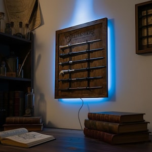 May include: A wooden display case with six wands, illuminated by a blue LED light. The case is branded with the text "Ollivanders" and is mounted on a wall. The wands are of various designs and colors, displayed on black rods.