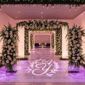 May include: A wedding ceremony entrance decorated with white flowers and greenery. The floor is illuminated with a pink monogram of the letters "E & Y" surrounded by a wreath.