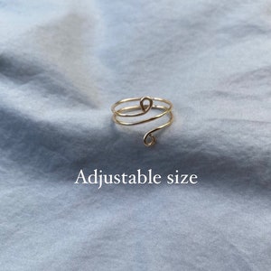 May include: A gold-toned adjustable ring with a spiral design. The ring is made of wire and has a small loop at the end.