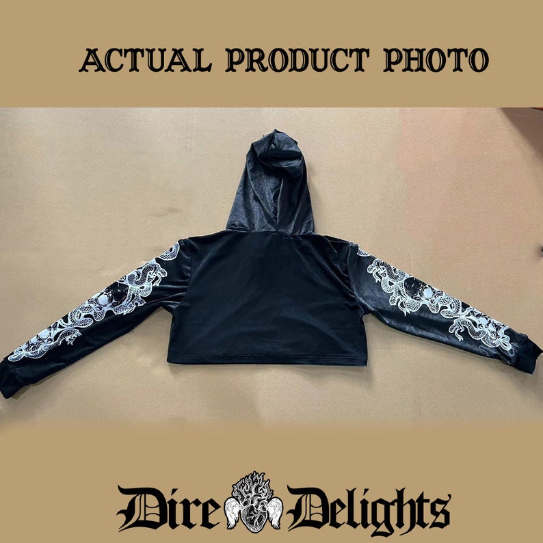 May include: Black cropped hoodie with a white graphic print of a skull and snakes on the sleeves. The hoodie has a drawstring hood and a relaxed fit.
