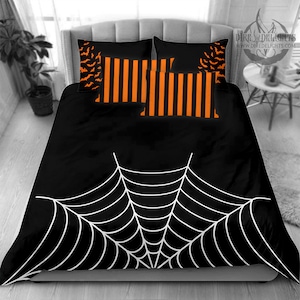 Könnte beinhalten: Schwarze und orangefarbene gestreifte Kissenbezüge mit einem schwarzen und weißen Spinnennetz-Design auf dem Bettbezug. Der Bettbezug hat ein großes weißes Spinnennetz-Design auf schwarzem Hintergrund.