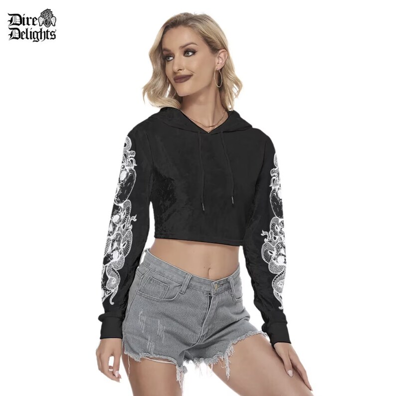 May include: Black cropped hoodie with long sleeves featuring a white snake design on the sleeves. The hoodie has a drawstring hood.