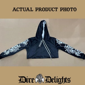 May include: Black cropped hoodie with a white skull and snake design on the sleeves. The hoodie has a drawstring hood and a tag that says "Dire Delights".
